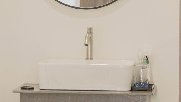Un baño con un espejo redondo, un lavabo blanco y un panel de madera en la pared.