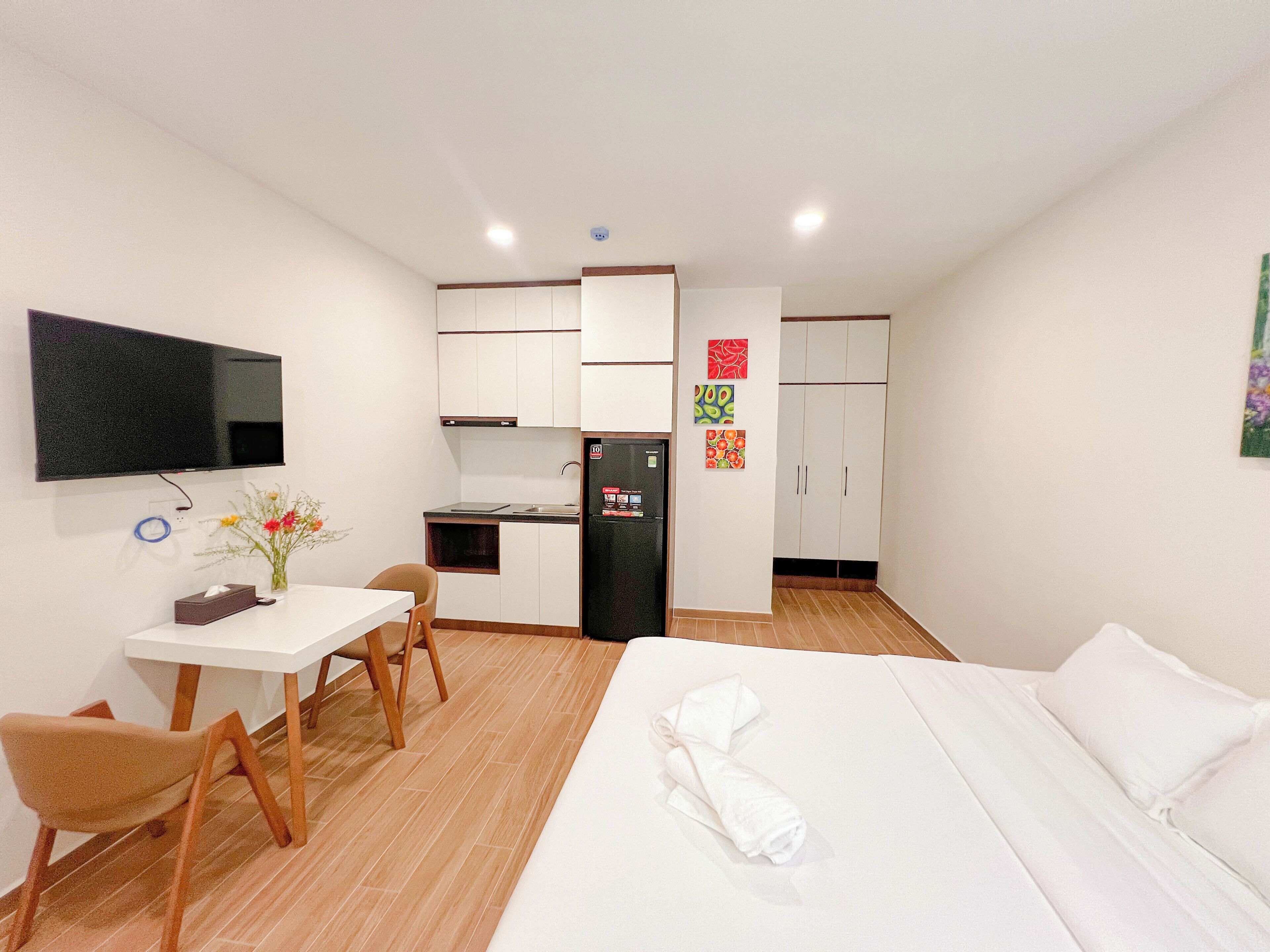 Ein kleines Hotelzimmer mit Bett, Schreibtisch, Stuhl, Fernseher, Kühlschrank und einer Küchenzeile.