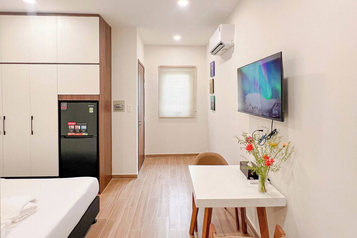 Ein kleines Hotelzimmer mit Bett, einem kleinen Tisch mit Stuhl, einem an der Wand montierten Fernseher und einem Kühlschrank.