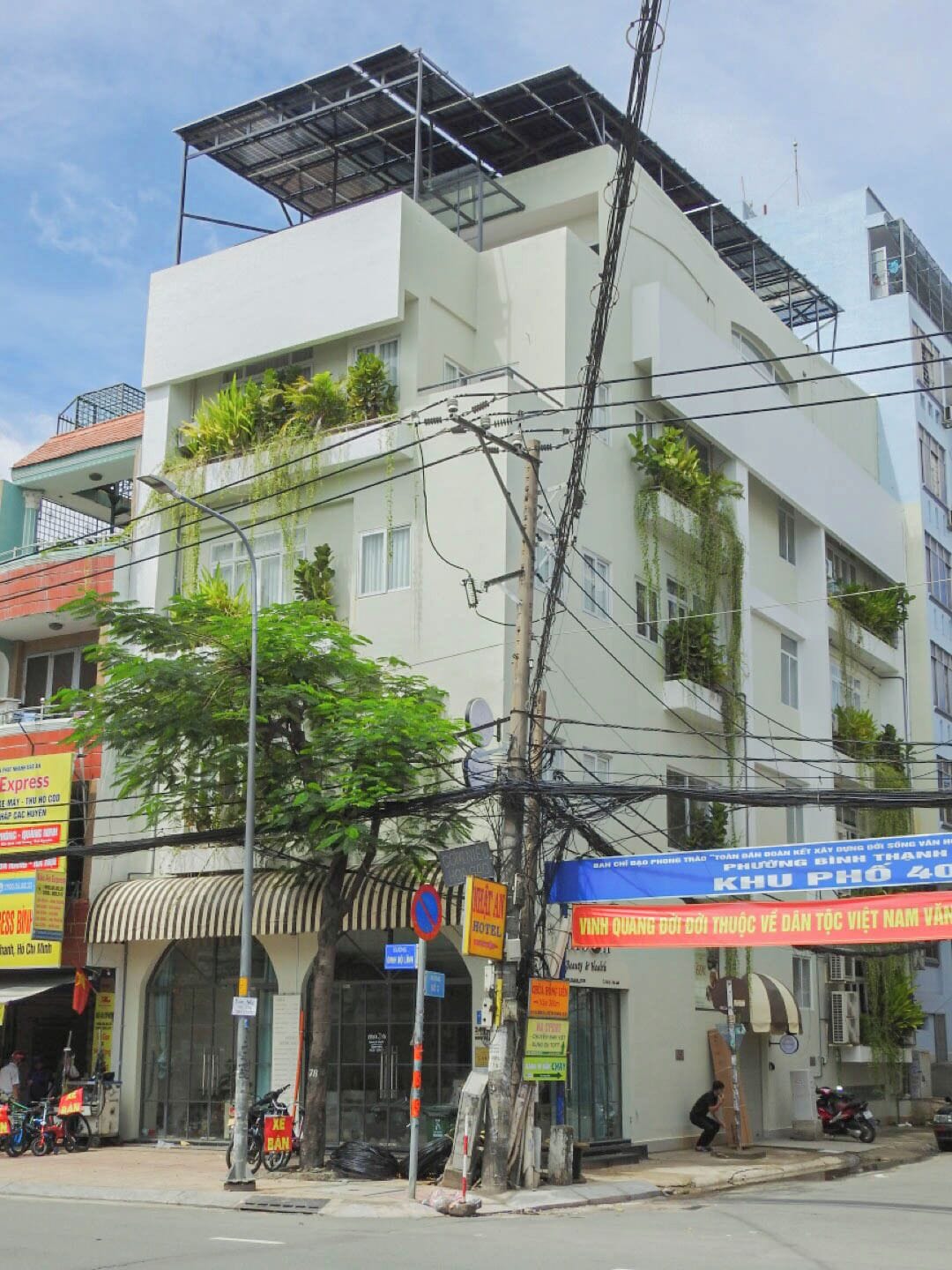 A multi-story building with a flat roof, balconies with plants, and various signs including a hotel and a bank.