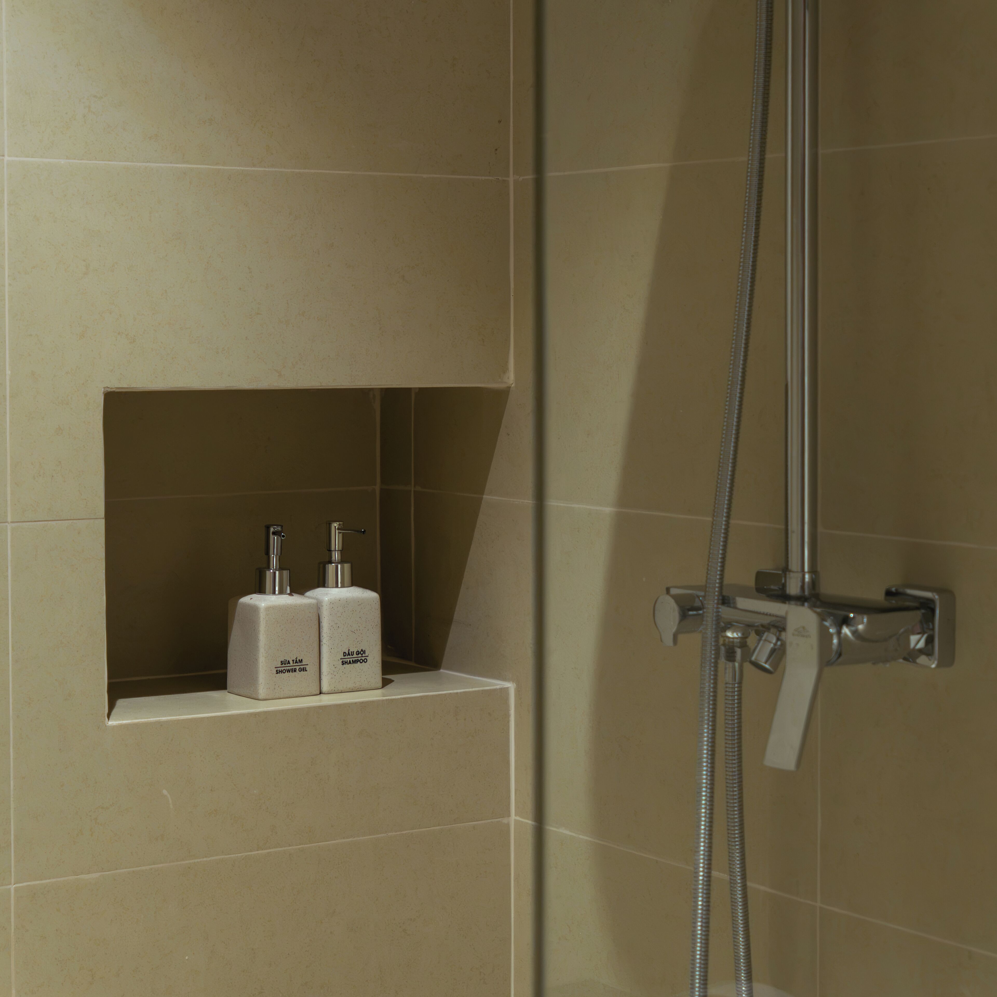 Een badkamer met een douche, een plank met twee flessen met de aanduiding 'douchegel' en 'shampoo', en een douchekop.