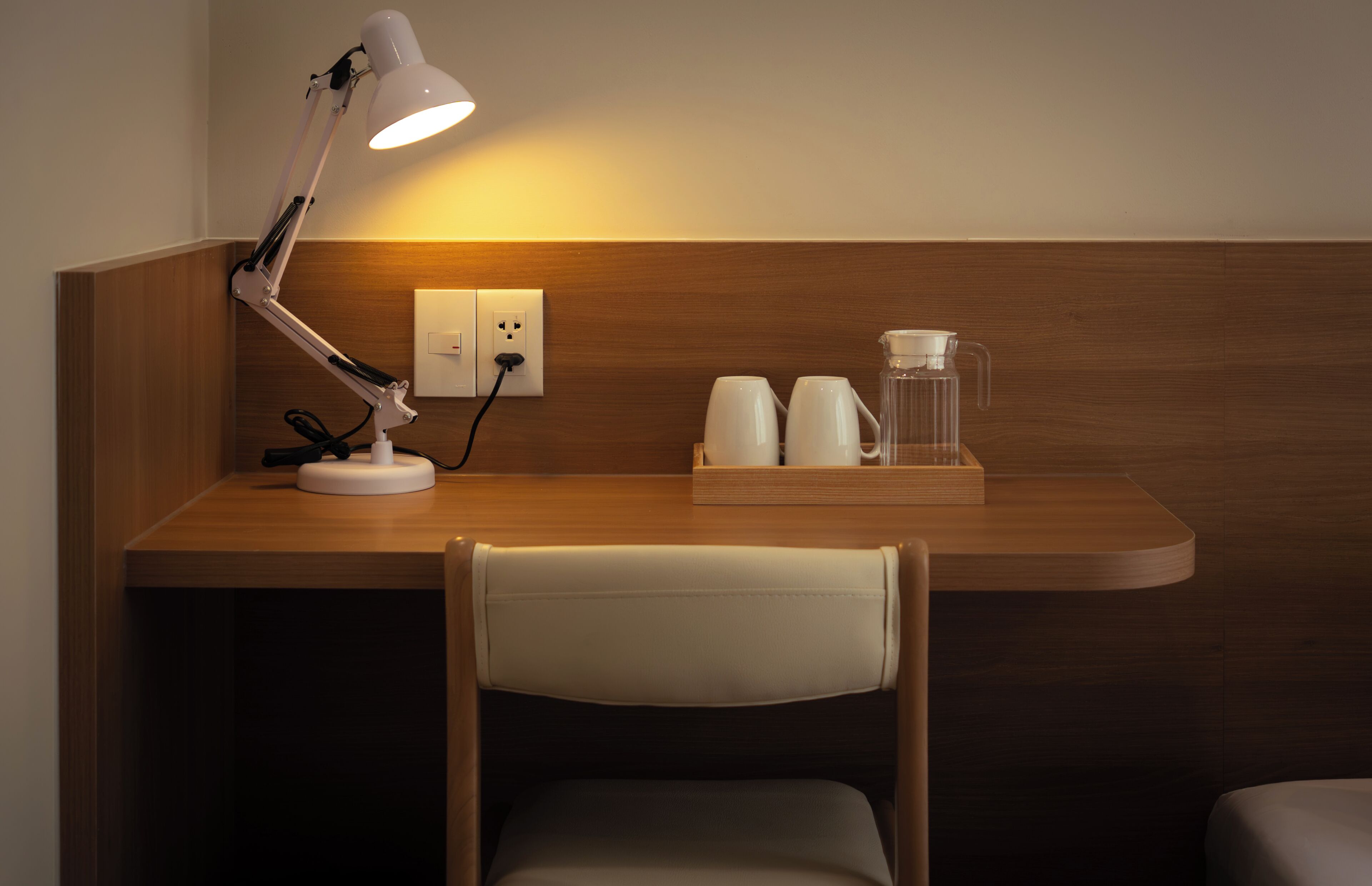 Un escritorio de madera con una lámpara de escritorio blanca, una cafetera y dos tazas blancas.