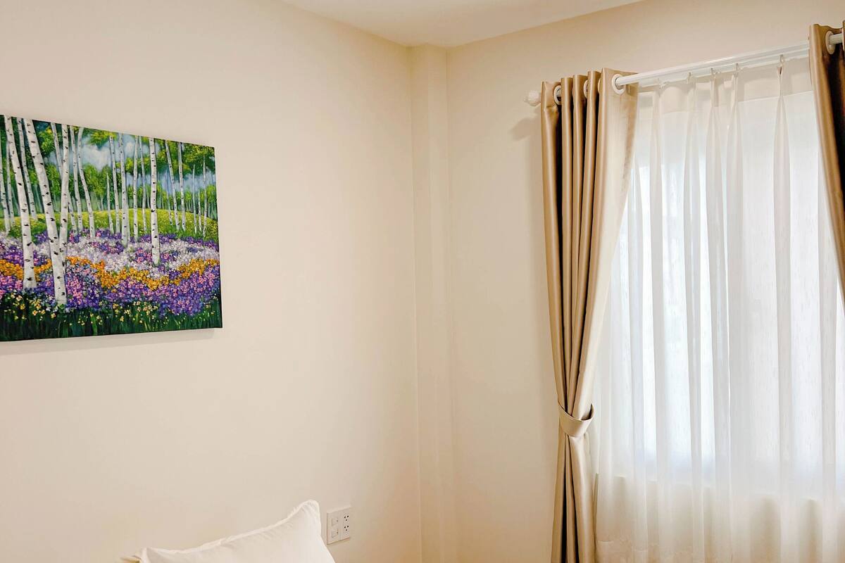 Ein Hotelzimmer mit Bett, einem Waldgemälde und einem Vorhangfenster.