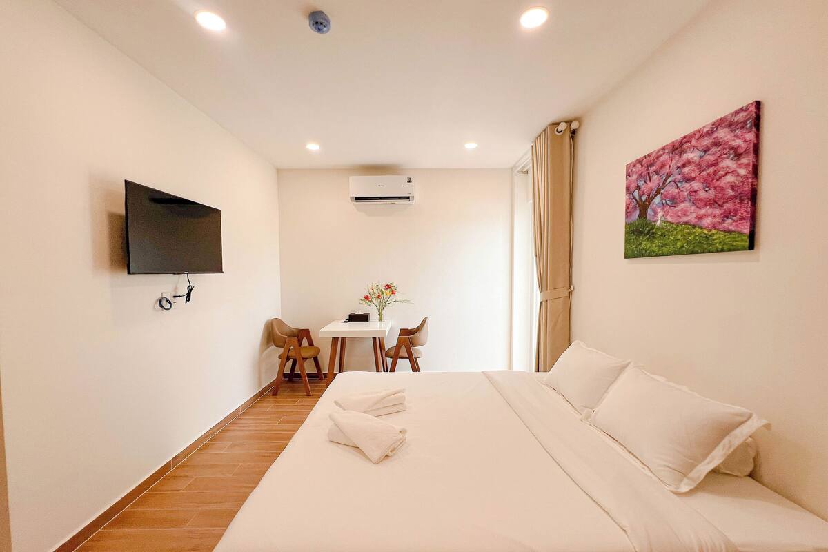 Ein Hotelzimmer mit einem Bett, einem an der Wand befestigten Fernseher, einem Schreibtisch mit Stühlen und einem Bild an der Wand.