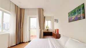 Una camera d'albergo con un letto grande, un balcone con tende e un quadro appeso al muro, con vista sulla città.