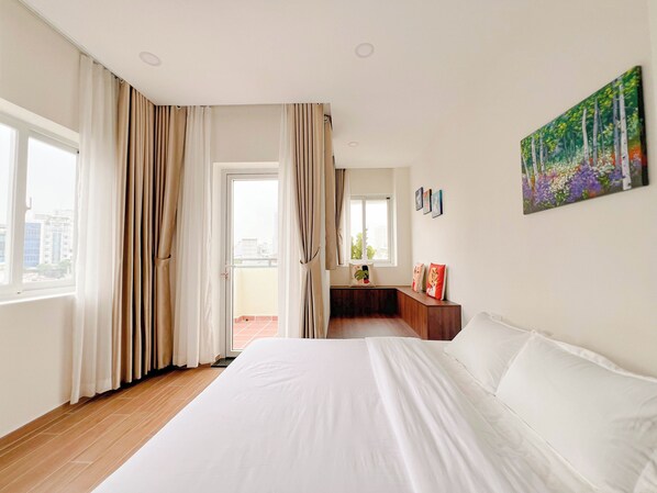 A hotel room with a large bed, a balcony with curtains, a painting on the wall, and a view of the city.