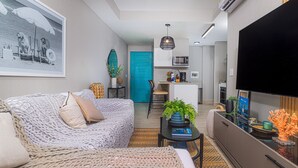 Una sala moderna con sofá, una mesa de centro con una planta, y un área de cocina con microondas y televisor.