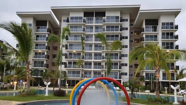 Un hotel con piscina, palmeras y un edificio de varios pisos con balcones.