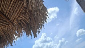 A beach scene with a palm tree and a thatched structure. - Stunning Oceanfront Apartment in Playa Caracol · Chame · Panama (Provincia de Panamá Oeste)