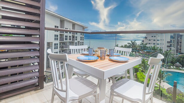 A balcony with a table set for two, overlooking a pool and a view of the ocean. - Stunning Oceanfront Apartment in Playa Caracol · Chame · Panama (Provincia de Panamá Oeste)