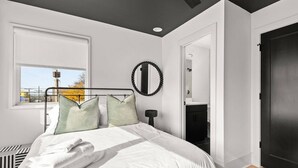 Un dormitorio moderno con una cama, una lámpara de noche, un espejo redondo y vistas al exterior.