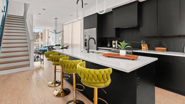 Una cocina moderna con una isla central, armarios negros y taburetes de bar verdes.