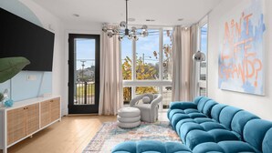 Una sala de estar moderna con un sofá azul, un sillón blanco y un ventanal con cortinas.