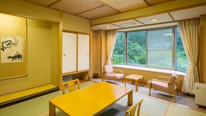 Una habitación tradicional japonesa con suelo de tatami, una mesita baja y vistas al verdor exterior.