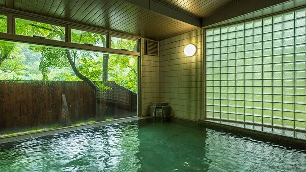 Un onsen japonés tradicional con interior de madera, vista a exuberante vegetación y pared de azulejos.