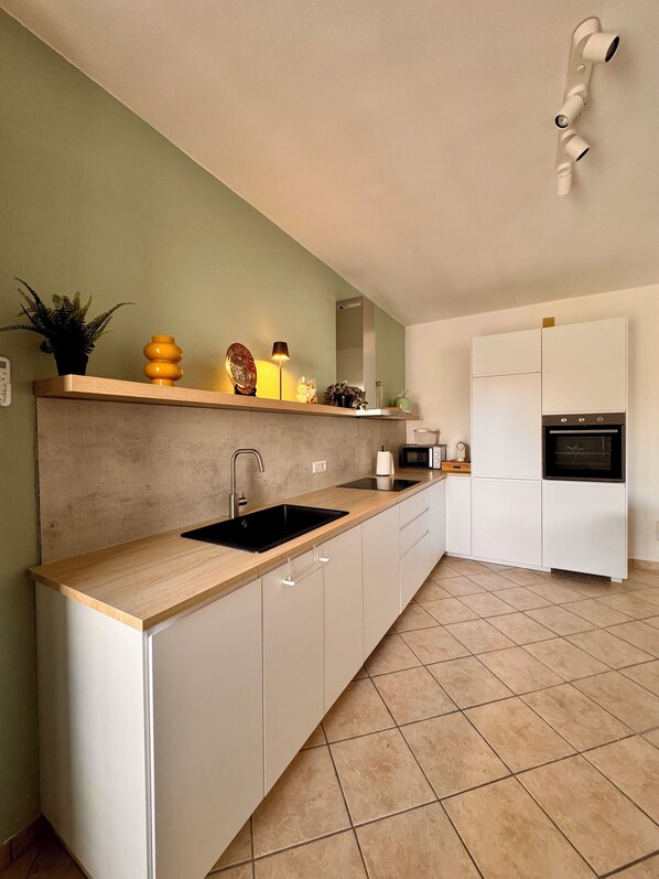 A modern kitchen with a wooden countertop, white cabinets, a built-in oven, and a microwave. - Villa with 3 rooms and garden among nature, sea, mountains (Tortolì)