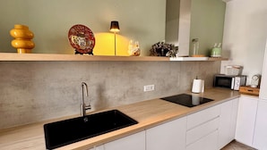 A modern kitchen with a wooden countertop, a black sink, white cabinets, and a green wall.