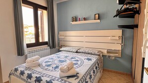 A bedroom with a bed, a window, a headboard, a shelf with items, and a radiator.