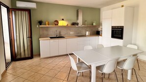 A modern kitchen with white cabinets, a built-in oven, and a dining area with a white table and chairs.