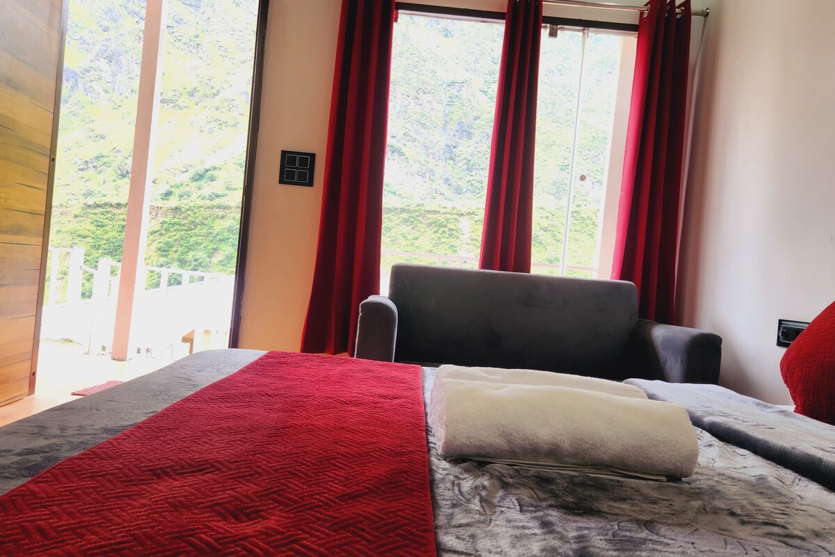 Una habitación con cama, una silla y un ventanal con cortinas rojas.