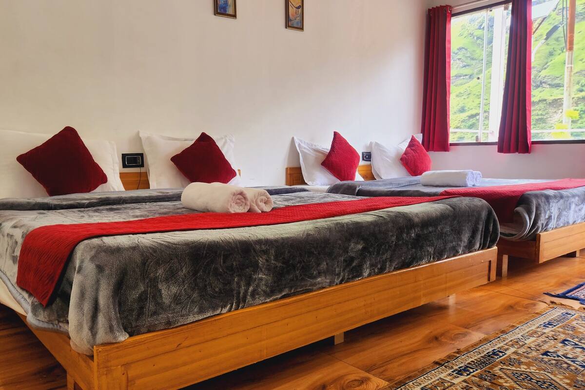 Cama doble con ropa de cama roja y gris, cabeceros de madera y una manta roja.