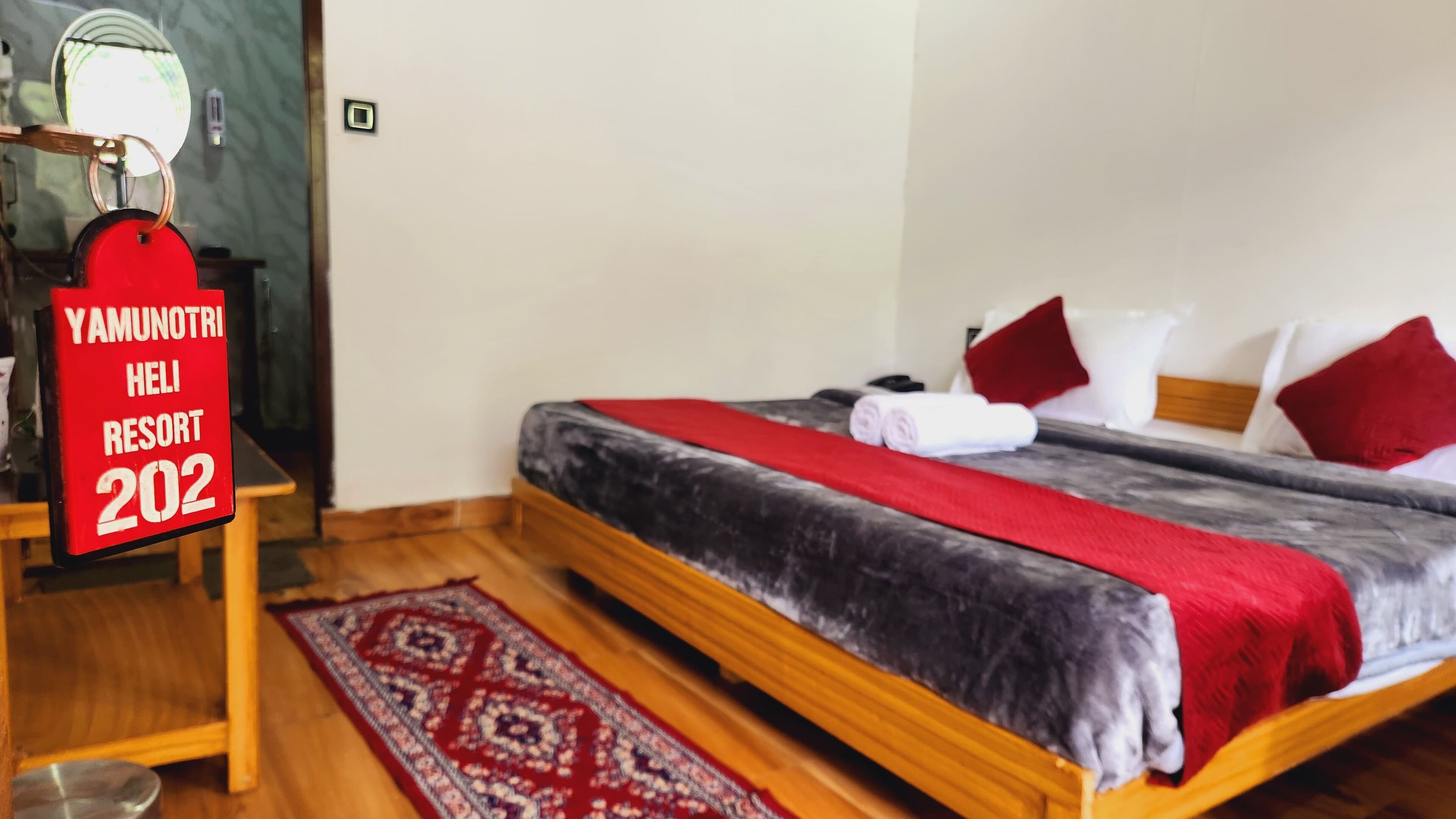 Une chambre d’hôtel avec un lit, des oreillers, un panneau rouge, un plancher en bois et un tapis à motifs.