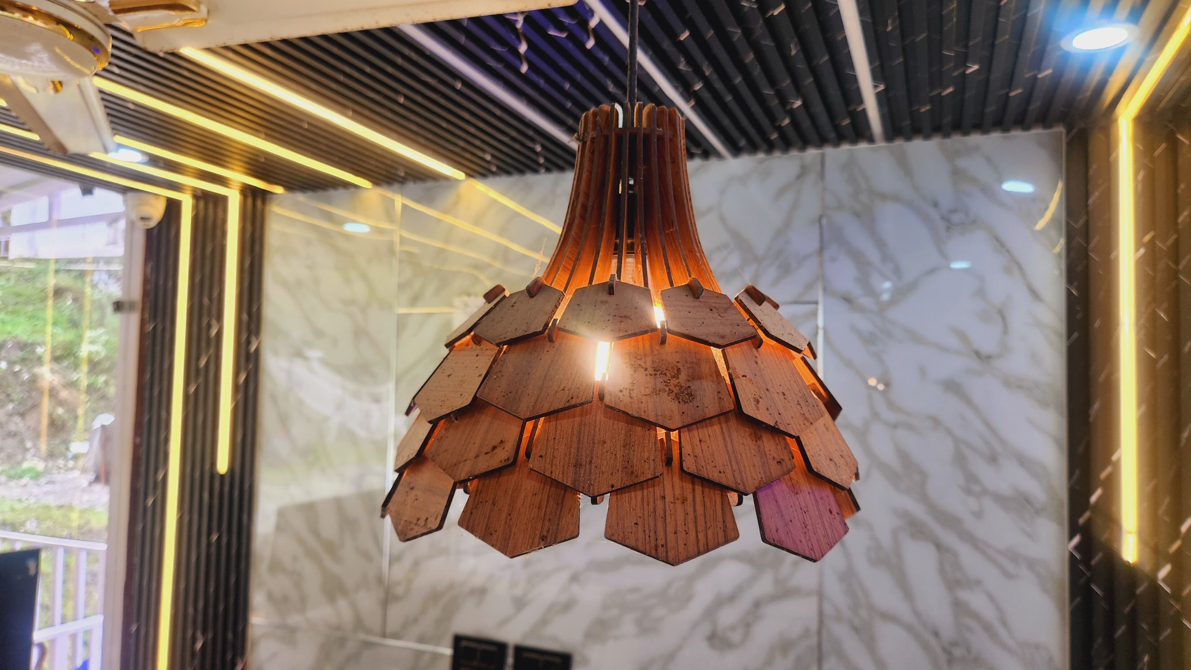 Un candelabro moderno con diseño geométrico, colgado en una habitación con paredes de mármol y un techo contemporáneo.