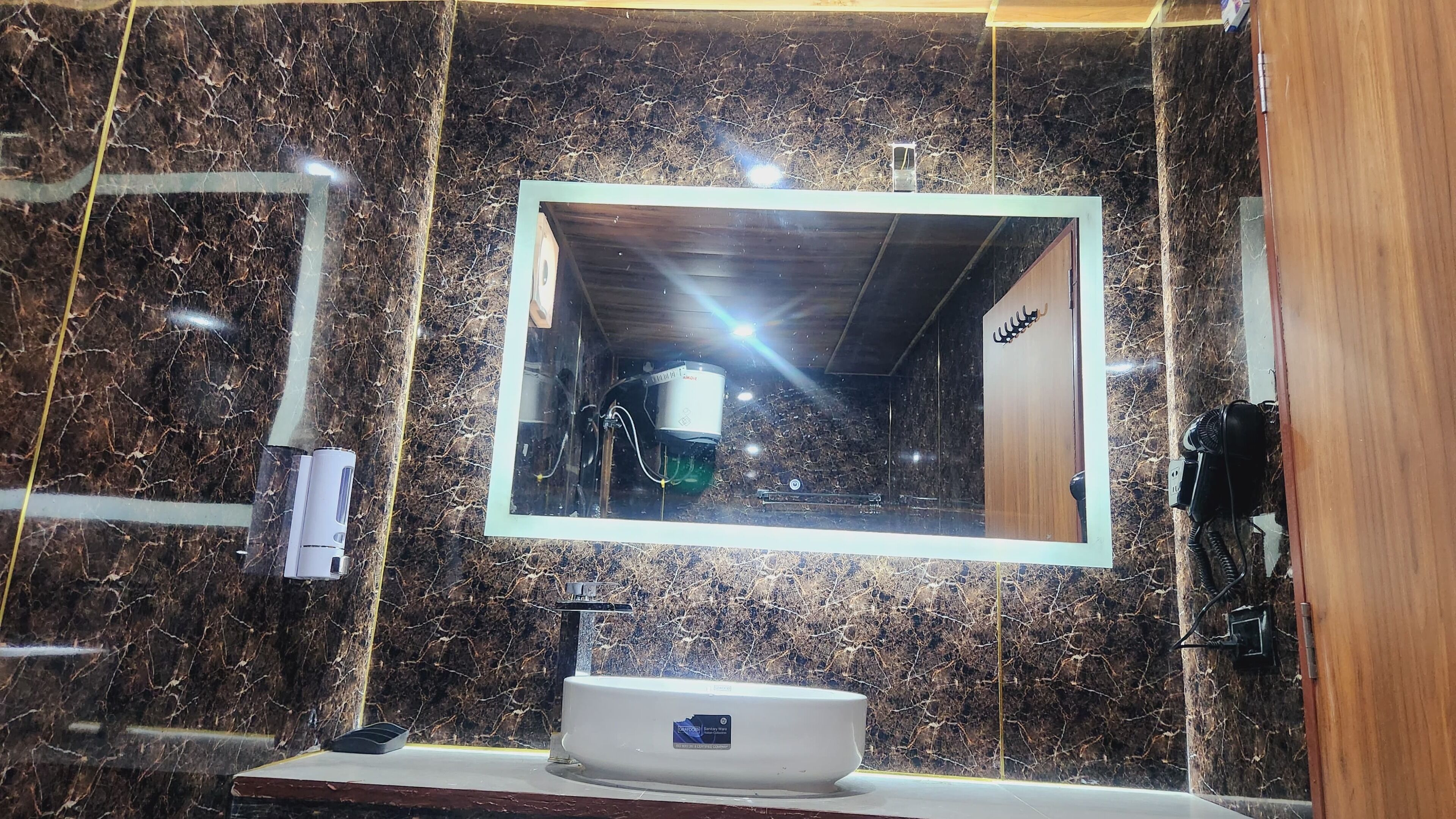 A bathroom with a marble wall, a sink with a mirror, and a hairdryer on the wall.