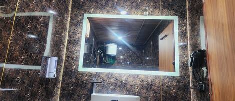A bathroom with a marble wall, a sink with a mirror, and a hairdryer on the wall.