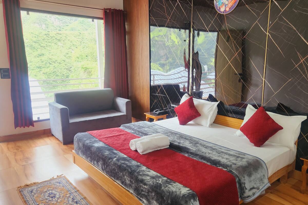 Habitación de hotel con una cama grande, un sofá, una mesita y vistas a zonas verdes.