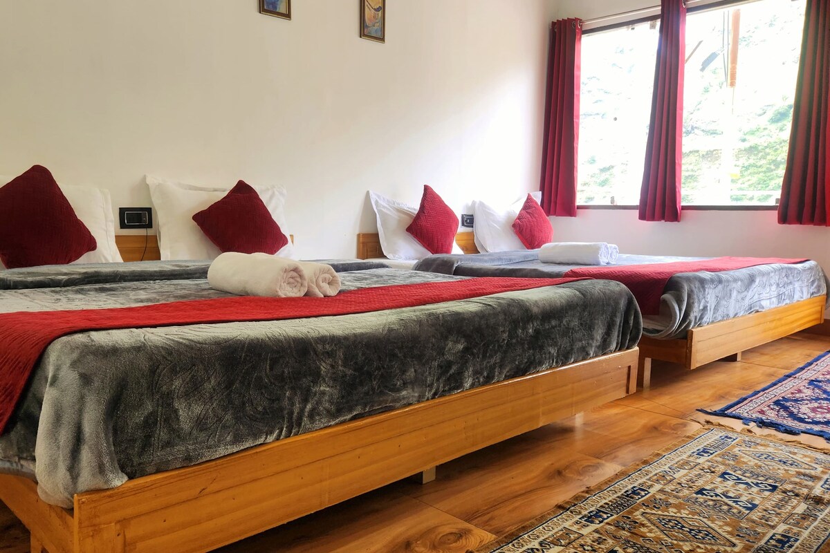 A hotel room with two wooden beds, red and white bedding, and a large window with red curtains.