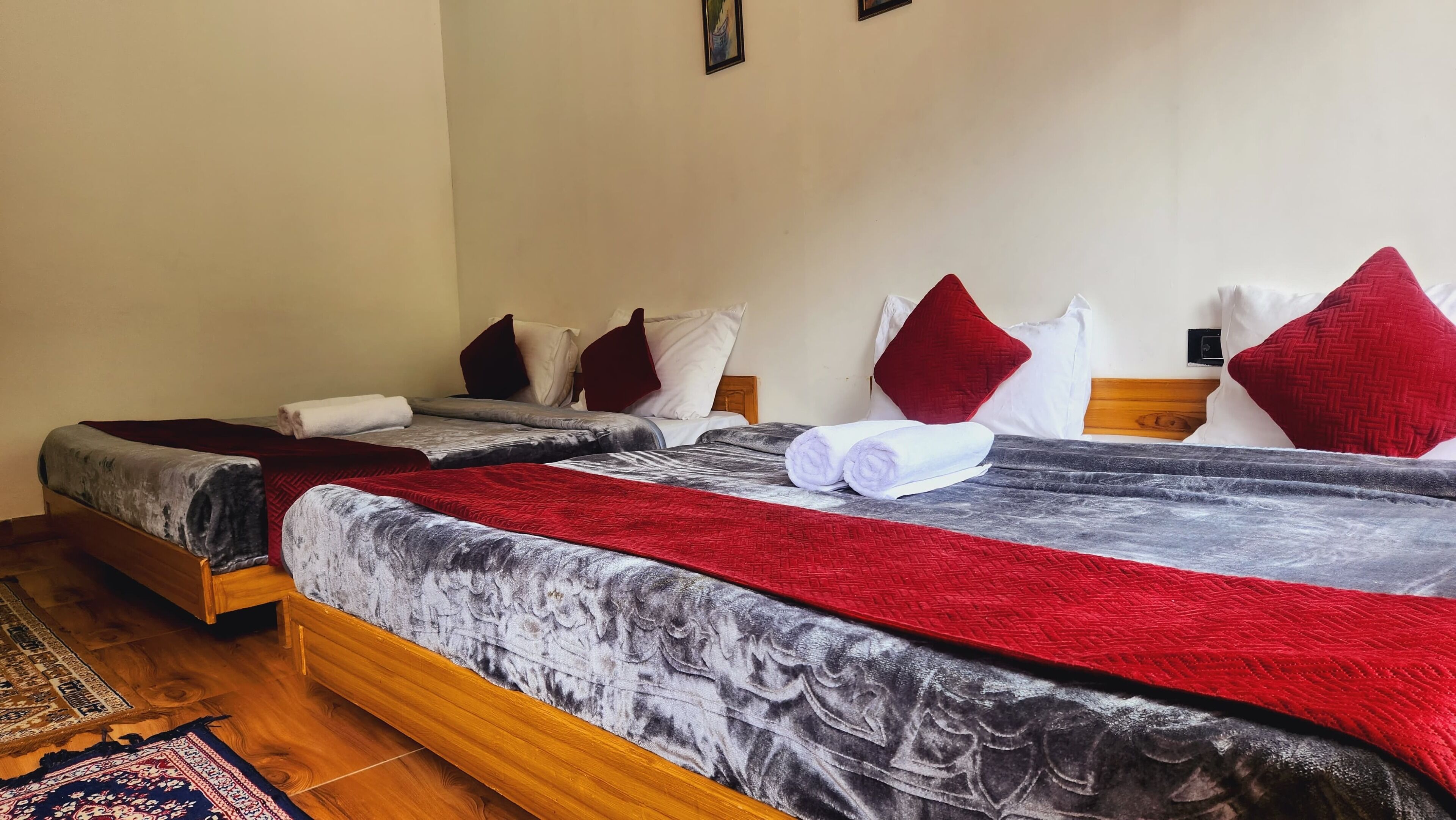 A double bed with a red and grey blanket, two pillows, and a wooden headboard.