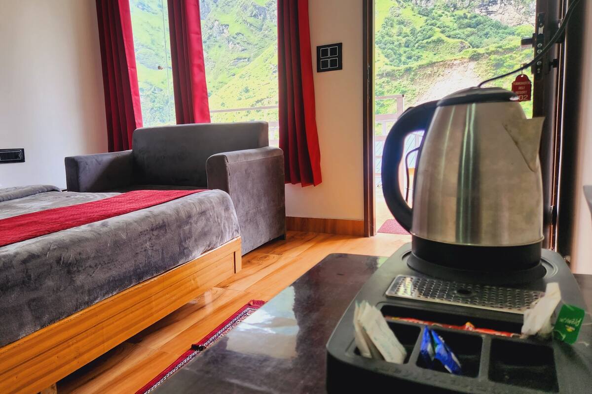 Habitación de hotel con cama, sofá, cafetera y vistas a un paisaje montañoso.