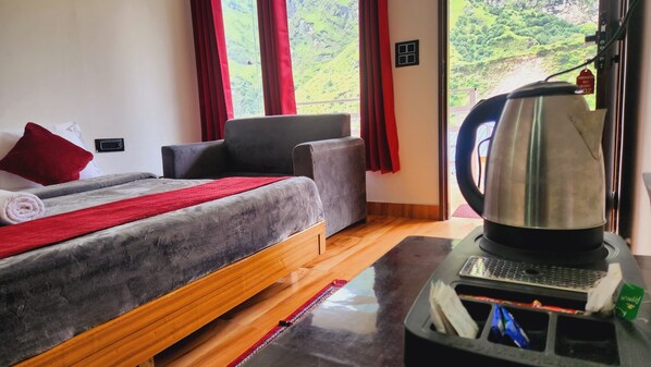 Habitación de hotel con cama, sofá, cafetera y vistas a un paisaje montañoso.