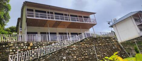 Un bâtiment à deux étages doté d’un balcon, d’un mur de soutènement en pierre et d’une clôture blanche.