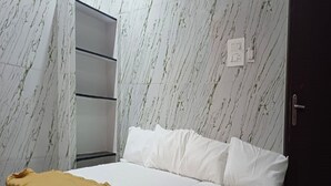 A bedroom with a bed, white bedding, a mustard-colored throw blanket, a wardrobe, and a marble-patterned wall. - Sun Shine Guest House (Puducherry)