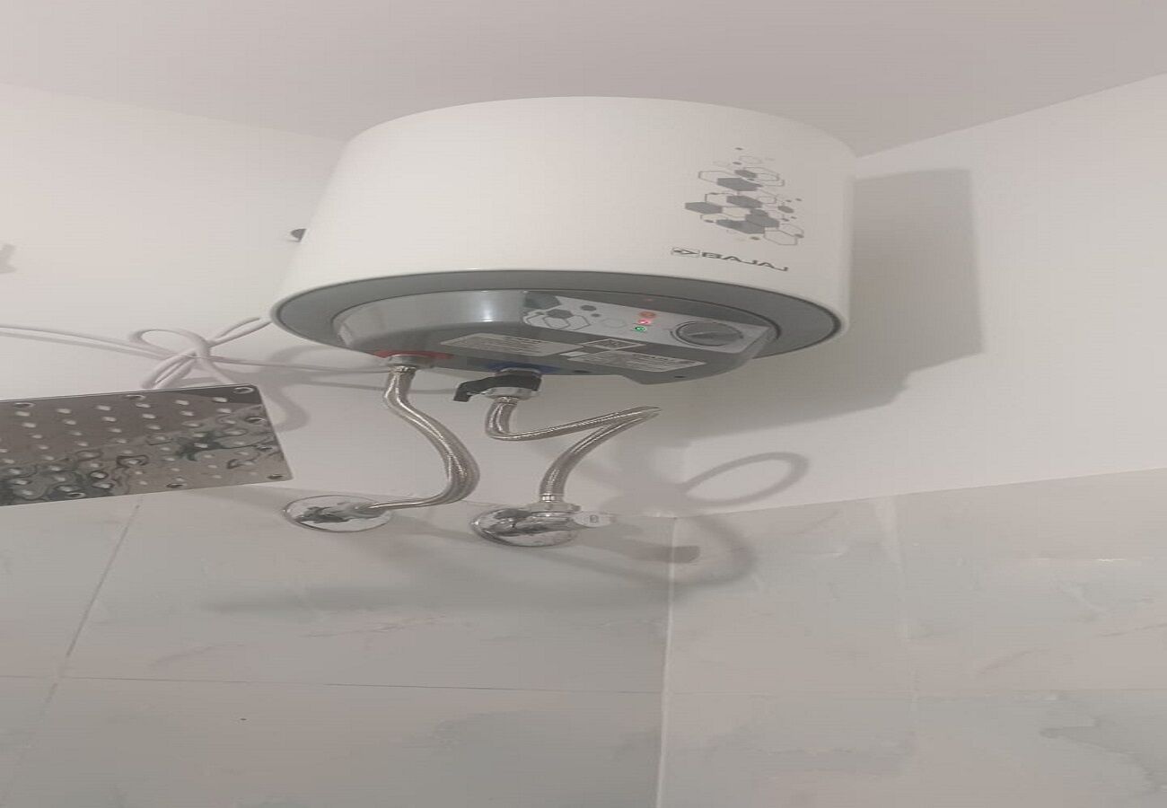 Ein an der Decke befestigter Boiler mit Bedienfeld, verbunden mit einem an der Wand montierten Heizkörper.