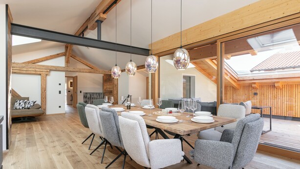 A dining area with a wooden table set for six, surrounded by grey upholstered chairs.