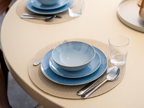 Une table dressée avec des assiettes bleues, un verre transparent et des couverts sur un set de table beige.