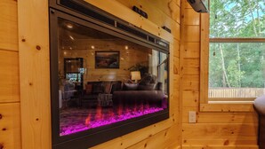 L’intérieur d’un chalet en bois, avec une cheminée, un canapé et une fenêtre donnant sur une forêt.
