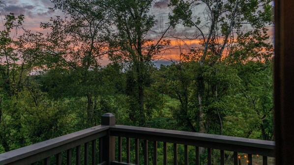 A view from a wooden deck overlooking a forest with a sunset in the background. - Hot tub, fire pit, foosball, arcade in the woods (Sevierville)
