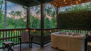 A covered outdoor area with a hot tub, wooden deck, and seating. - Hot tub, fire pit, foosball, arcade in the woods (Sevierville)