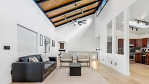 Ein geräumiges Wohnzimmer mit hoher Decke, einem schwarzen Ledersofa, einem beigefarbenen Sessel und einem Couchtisch.