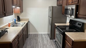 A compact kitchen with wooden cabinets, a stainless steel refrigerator, a microwave, a stove, and a sink. - Hampton vacation home near Langley AFB (Hampton)