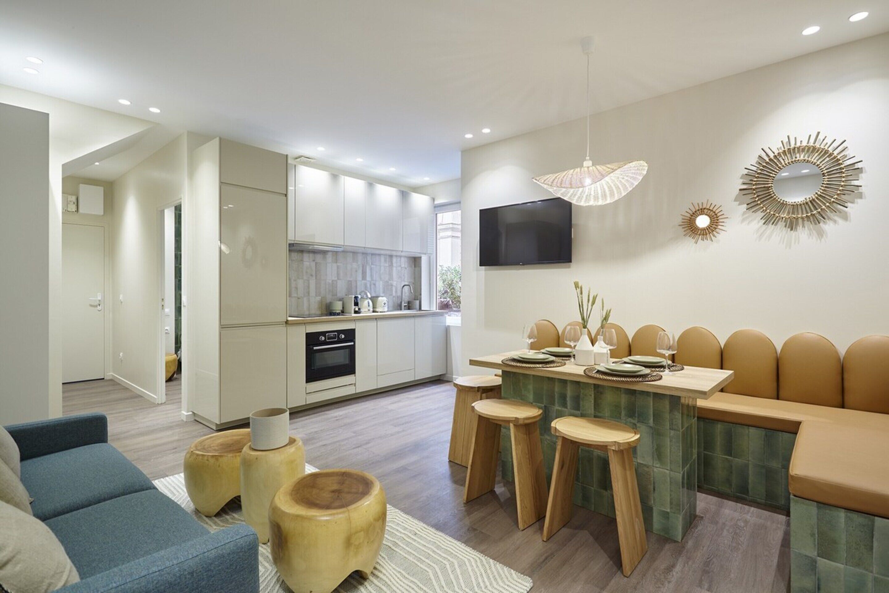 A modern kitchen with white cabinets, a dining area with stools, and a TV mounted on the wall.