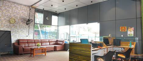 A modern office space with a brown leather sofa, a wooden coffee table, and a desk area with computers and chairs.