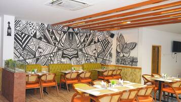 A restaurant with a geometric patterned wall, wooden ceiling beams, and orange seating.