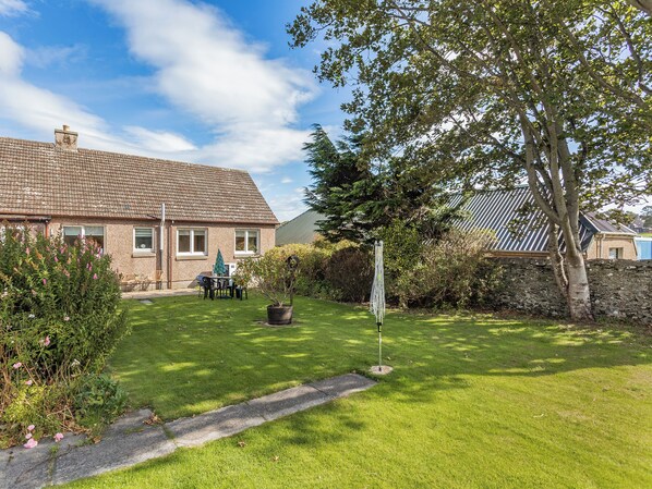 A house with a tiled roof, a lawn, and a garden with a tree and flowers.