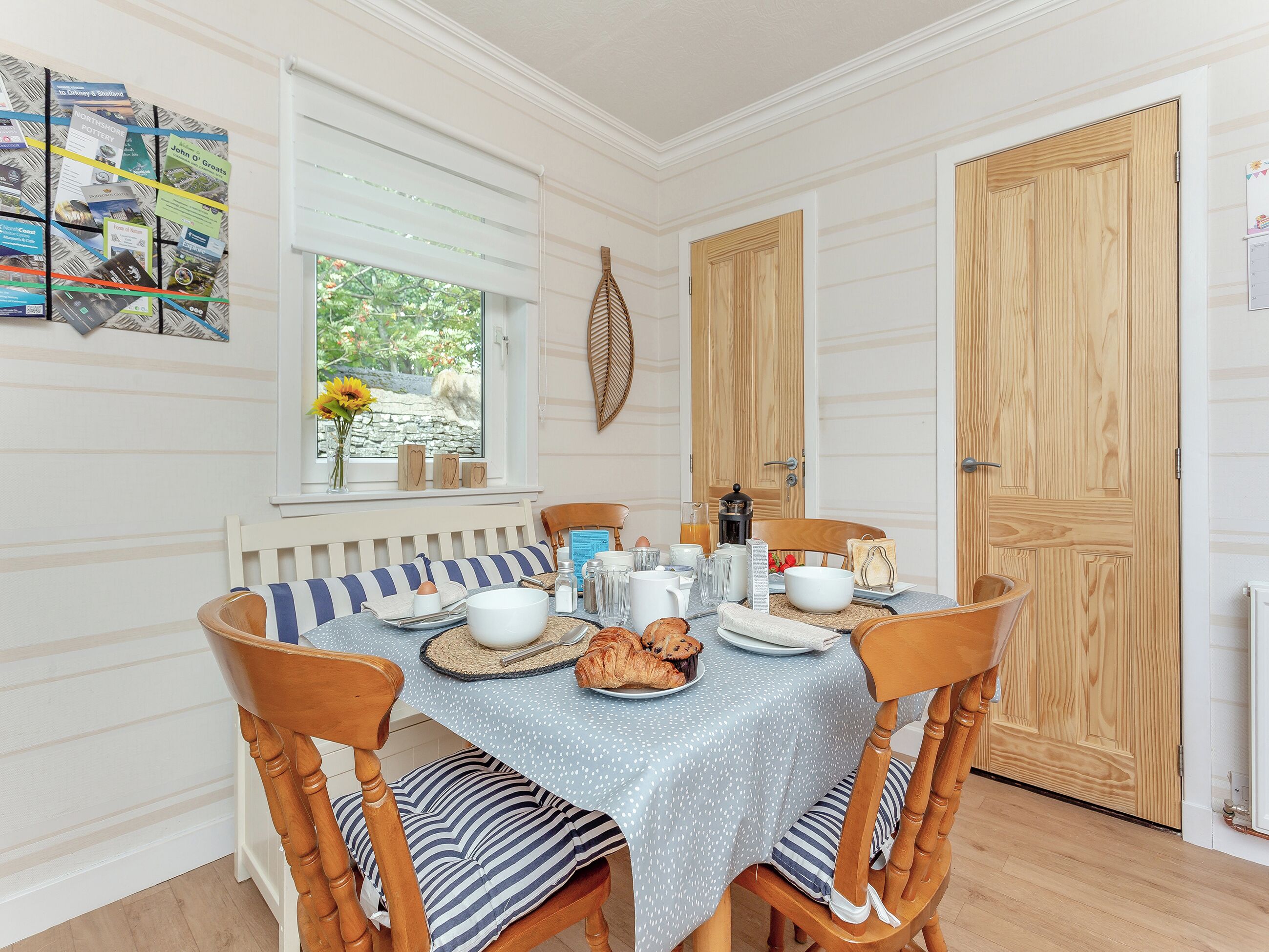 Un comedor con una mesa redonda para cuatro personas, sillas de madera, mantel azul y una ventana con persianas.
