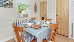 A dining area with a round table set for four, wooden chairs, a blue tablecloth, and a window with blinds.